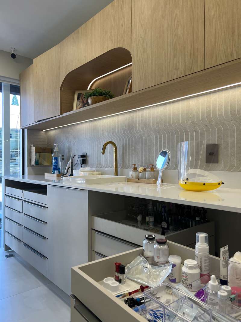 Detalhe de bancada clínica com torneira dourada, revestimento ondulado e gaveta aberta com materiais separados
